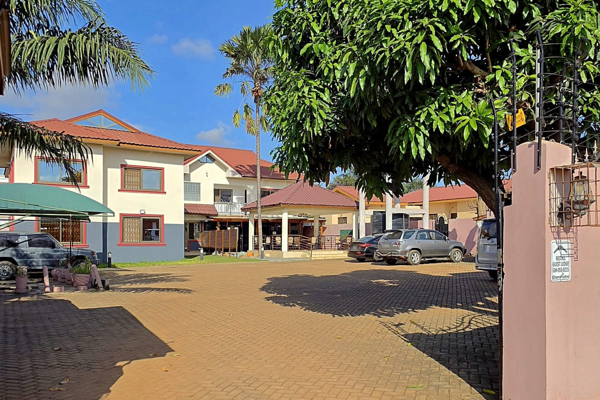 Through the gate of Restall Guest Lodge: the compound, the car park, and the building under a mango tree