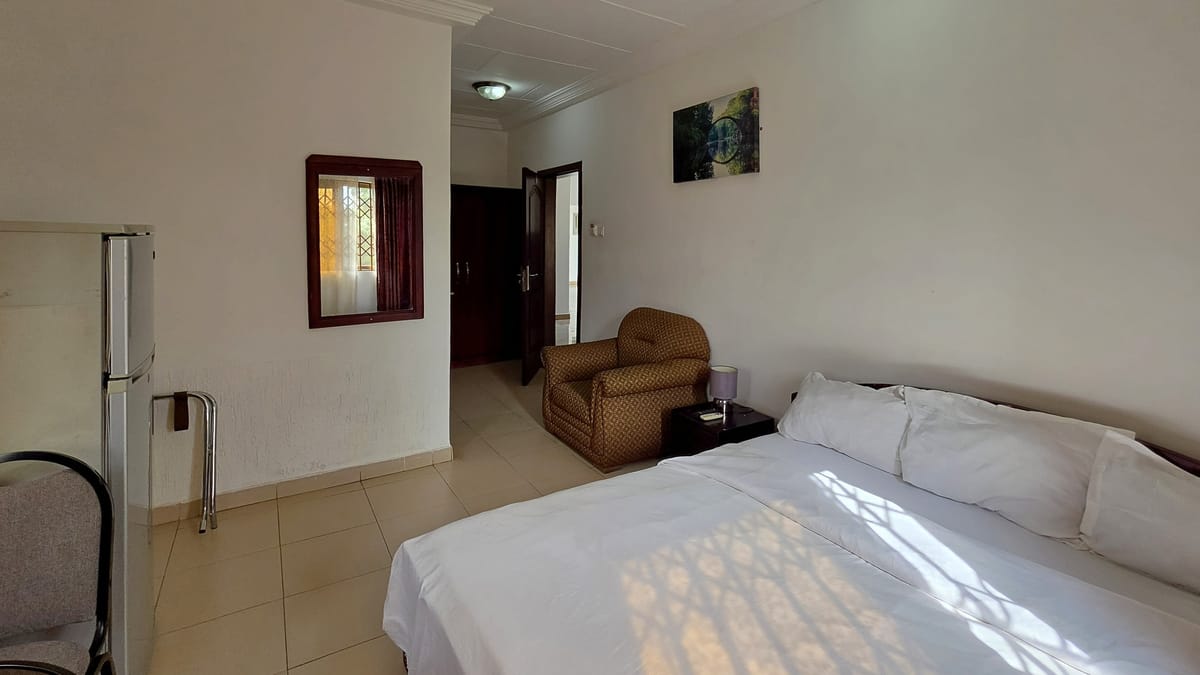 A Standard Room with a queen bed, an armchair, and a fridge